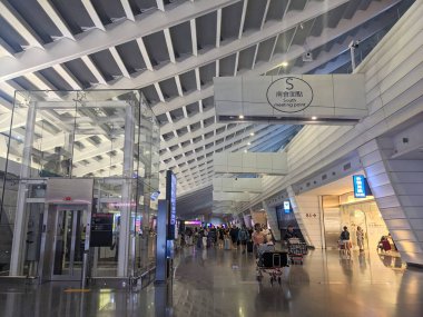 Taipei, Tayvan - 22 Mayıs 2025: Bagaj arabalı gezginler modern mimari ve cam asansörle Tayvan Uluslararası Havalimanı 'nın hareketli varış salonlarında yürüyorlar