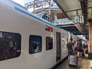 Hualien, Tayvan - 23 Mayıs 2025: Bavul taşıyan yolcular güneşli bir günde yolculukları için modern bir Tayvan Demiryolları İdaresi ekspres treninden çıktıktan sonra istasyon platformu boyunca yürüyorlar