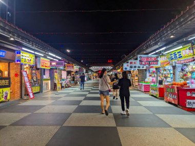 Hualien, Tayvan - 23 Mayıs 2025: İnsanlar Dongdamen Gece Pazarı 'nın kareli kaldırımlarında canlı gıda tezgahlarını ve renkli neon levhalarla aydınlatılan oyun dükkanlarını keşfediyorlar.