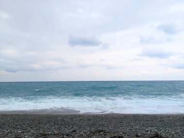 Hualien, Tayvan - 25 Mayıs 2025: Turkuaz okyanus dalgaları Qixingtan 'da, ufukta geniş, karamsar ve bulutlu bir gökyüzü olan koyu çakıl taşlarıyla karşılaştıklarında beyaz köpük oluşturur.