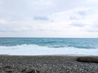 Hualien, Tayvan - 25 Mayıs 2025: Güçlü bir okyanus dalgası Qixingtan 'da, engebeli kıyılarda engin ve karamsar bulutlu bir gökyüzünün altında, yıpranmış bir kayalık ile birlikte karanlık bir çakıl taşı kumsalında kırılır.