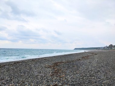 Hualien, Tayvan - 25 Mayıs 2025: Pasifik Okyanusu 'nu Chishingtan Sahili' nin engin çakıl taşlı kıyılarından sürüklenen bir şahıs dramatik bulutlu bir gökyüzü altında kıyı şeridi boyunca yayılmış bir dalgadır.