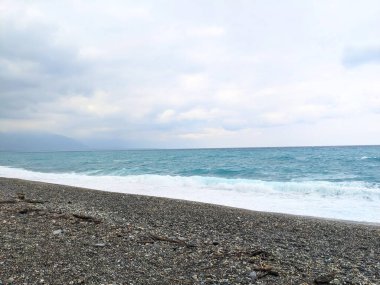 Hualien, Tayvan - 25 Mayıs 2025: Turkuaz Pasifik Okyanusu üzerinde bulutlu gökyüzü dalgalar Qixingtan 'da bir çakıl taşı plajına çarpıyor.