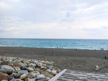 Hualien, Tayvan - 25 Mayıs 2025: Ziyaretçiler, büyük bulutlu bir gökyüzünün altında turkuaz Pasifik Okyanusu dalgalarının karanlık kumla buluştuğu ünlü Qixingtan Sahili 'nin geniş çakıl taşlı kıyı şeridinin tadını çıkarıyorlar.