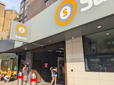 Glasgow, İskoçya, İngiltere - 13 Temmuz 2025: İnsanlar, aydınlık bir yaz gününde Hillhead metro istasyonu modern girişine yürürler ve içeri girerler.