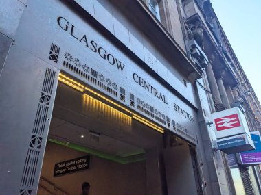 Glasgow, İngiltere - 13 Temmuz 2025: Düşük açılı bir perspektif, tarihi Glasgow Merkez İstasyonu 'nun modern aydınlatma girişini ve Ulusal Demiryolu işaretini açık bir gökyüzüne yansıtıyor