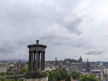 Edinburgh, İskoçya - 15 Temmuz 2025: Calton Hill 'den yükselen manzara Dugald Stewart Anıtı' nı Edinburgh Şatosu 'nun da içinde bulunduğu tarihi Eski Şehir silueti ile birlikte bulutlu bir gökyüzü altında gösteriyor