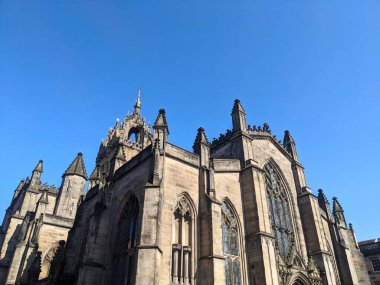 Edinburgh, İskoçya - 16 Temmuz 2025: Düşük açılı bir manzara, açık mavi gökyüzüne karşı St. Giles Katedrali 'nin karmaşık Gotik cephesini ve taç çan kulesini yakalar