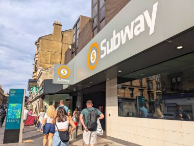 Glasgow, İskoçya, İngiltere - 13 Temmuz 2025: İnsanlar Byres Yolu 'ndaki kaldırım boyunca, şehrin canlı West End semtindeki Hillhead metro istasyonunun modern girişine doğru yürüyorlar.