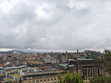 Edinburgh, İskoçya - 15 Temmuz 2025: Kapsamlı bir şehir manzarası tarihi Eski Şehir mimarisini ve Edinburgh Kalesini yoğun ve bulutlu bir gökyüzünün altındaki bir tepede sergiliyor