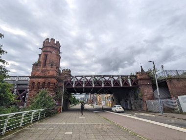 Glasgow, İngiltere - 14 Temmuz 2025: Tarihi kırmızı kumtaşı Union Demiryolu Köprüsü 'nün altındaki kaldırımda bulutlu bir günde Victoria döneminden kalma kendine has kuleleriyle bir yaya yürüyor