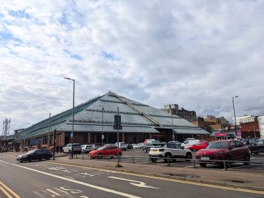 Glasgow, İngiltere - 14 Temmuz 2025: Arabalar, bulutlu mavi gökyüzü altında belirgin cam piramit çatısı bulunan büyük bir perakende satış noktası olan modern St Enoch Center 'ın önündeki bir şehir otoparkında oturuyorlar