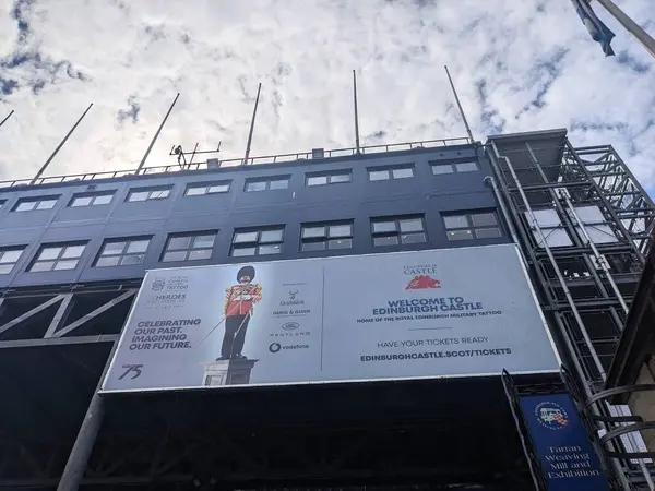 Edinburgh, İngiltere - 16 Temmuz 2025: Modern tribünün alçak açılı görüntüsü ve bulutların altında Edinburgh Kraliyet Askeri Dövmesi 'nin vatanı tarihi Edinburgh Şatosu' nun büyük reklam panosu