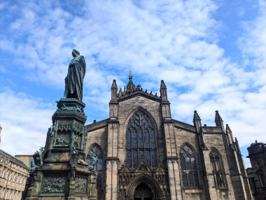 Edinburgh, İngiltere - 16 Temmuz 2025: Düşük açılı bir perspektif, tarihi Bükreş Anıtı 'nı ve St. Giles Katedrali' nin karmaşık dış görünüşünü mavi gökyüzü ve beyaz bulutlara karşı yansıtıyor