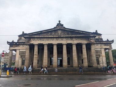 Edinburgh, İskoçya - 15 Temmuz 2025: Kraliyet İskoç Akademisi 'nin Neoklasik Girişi' nin tarihi şehir merkezinde bulutlu bir günde ıslak bir Princes Caddesi boyunca yürüyen yayalar görülüyor
