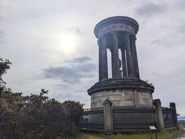 Edinburgh, İskoçya - 15 Temmuz 2025: Calton Hill 'de güneş bulutları arasından görünen atmosferik bulutlu bir gökyüzüne karşı ayakta duran ikonik neoklasik Dugald Stewart Anıtı