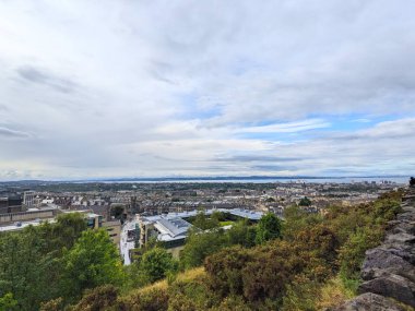 Edinburgh, İskoçya - 15 Temmuz 2025: Calton Hill 'den şehrin tarihi çatılarının üzerinden Forth' un Firth 'una doğru bulutlu bir gökyüzünün altındaki kayalık bir noktadan geniş bir yüksek açı görüntüsü
