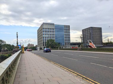 Glasgow, İskoçya - 14 Temmuz 2025: Trafik tarihi Albert Köprüsü 'nü geçerek Clyde Nehri üzerinden Glasgow Üniversitesi Riverside Kampüsü' nün modern cephesine ulaşır.