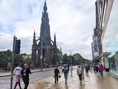 Edinburgh, İskoçya - 15 Temmuz 2025: Bulutlu bir günde Viktorya Dönemi Gotik Scott Anıtı 'nın yanındaki ıslak kaldırımda yürüyen yayalar eşliğinde Princes Caddesi' nde hareketli bir şehir manzarası