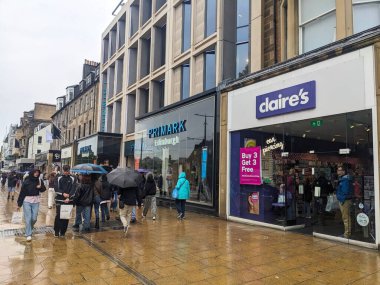 Edinburgh, İskoçya - 15 Temmuz 2025: Şemsiyeli kalabalık, modern ve geleneksel mimariyle birlikte büyük bir perakende caddesi olan Princes Caddesi 'nin ıslak kaldırımlarında yürüyor