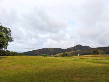 Edinburgh, İskoçya, İngiltere - 15 Temmuz 2025: Calton Hill 'den ikonik Arthurs Seat ve Salisbury Crags' ın geniş bir manzarası, yeşil tepeler ve çayırlarla kaplı geniş bir şehir parkı