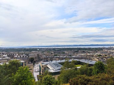 Edinburgh, İskoçya - 15 Temmuz 2025: Calton Hill 'den tarihi mimarisi ve Forth' un Firth of Forth ile şehir silueti üzerindeki geniş hava manzarası bulutlu bir gökyüzü altında