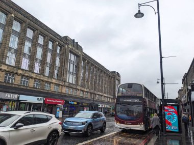 Edinburgh, İskoçya - 15 Temmuz 2025: Kırmızı çift katlı bir Lothian otobüsü, yağmurlu Fountainbridge 'de kaldırımda yayalar ile bulutlu bir gökyüzü altında geleneksel binaların önünden geçiyor.