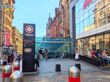 Glasgow, İskoçya - 12 Temmuz 2025: Banliyö ve turistler, tarihi Viktorya dönemi mimarisini yansıtan modern cam cepheli Buchanan Caddesi metro istasyonuna indiler