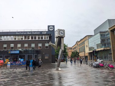 Glasgow, İskoçya - 15 Temmuz 2025: Çağdaş Saat heykeli ve Buchanan Otobüs İstasyonu girişi ile yürüyen insanlar şehir merkezinde yağmurlu ve bulutlu bir günde