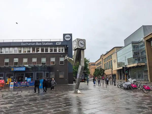 Glasgow, İskoçya - 15 Temmuz 2025: Çağdaş Saat heykeli ve Buchanan Otobüs İstasyonu girişi ile yürüyen insanlar şehir merkezinde yağmurlu ve bulutlu bir günde