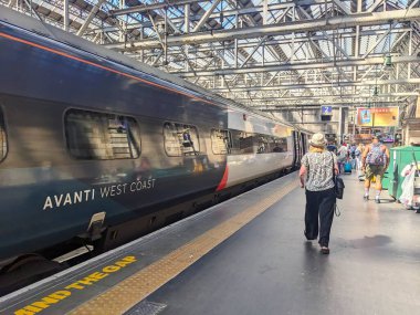 Glasgow, İskoçya - 12 Temmuz 2025: Gezginler şehir ve ülke için büyük bir ulaşım merkezi olan tarihi Merkez İstasyonu 'ndaki modern Avanti Batı Yakası treninin yanında platformda yürüyorlar