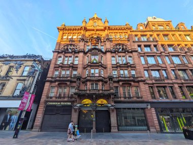 Glasgow, İskoçya - 12 Temmuz 2025: Argyll Arcade 'nin ikonik kırmızı kumtaşı Viktorya dönemi cephesi altın saat güneşinde yayalar ünlü alışveriş caddesinde gezinirken parlıyor