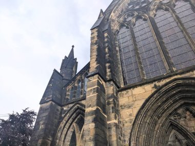 Glasgow, İskoçya, İngiltere - 14 Temmuz 2025: Tarihi Glasgow Katedrali 'nin alçak açılı görüntüsü, karmaşık ortaçağ Gotik mimarisini gözler önüne seriyor ve bulutlu bir gökyüzü altında yıpranmış taş cephe altında yıpranmış