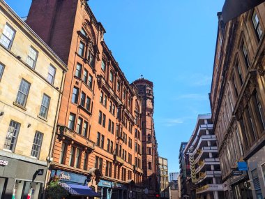 Glasgow, İngiltere - 12 Temmuz 2025: Parlak, güneşli bir günde açık mavi gökyüzü altında Gordon Caddesi 'ni çevreleyen tarihi kırmızı kumtaşı Victorian ve modern binaların düşük açılı perspektifi
