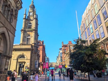 Glasgow, İngiltere - 12 Temmuz 2025: İnsanlar, tarihi St Georges Tron Kilisesi ile açık mavi gökyüzüne karşı popüler bir alışveriş merkezi olan Buchanan Caddesi boyunca yürüyor