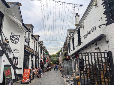 Glasgow, İskoçya - 13 Temmuz 2025: West End 'de barları, restoranları ve sicim lambalarıyla tanınan ünlü bir cadde olan Ashton Lane' deki kaldırımlı kaldırım taşlı restoranların ve yayaların canlı bir sahnesi