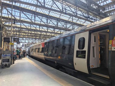 Glasgow, İngiltere - 12 Temmuz 2025: Modern bir Avanti Batı Yakası treninden indikten sonra platformda bavulu olan yolcular tarihi Central Station 'da Viktorya dönemi sembolik cam çatısının altında indiler.