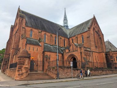 Glasgow, İskoçya - 14 Temmuz 2025: Yayalar bulutlu bir günde Strathclyde Üniversitesi 'nde, Barony Kilisesi olarak bilinen tarihi Baronluk Salonu' nun kırmızı kumtaşı Gotik cephesinin yanında yürürler