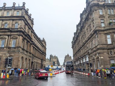 Edinburgh, İskoçya - 15 Temmuz 2025: Islak Princes Caddesi 'nde kırmızı çift katlı bir otobüs yağmurlu bir günde Balmoral Hotel' in yanındaki kaldırımda şemsiyeli yayalar beklerken