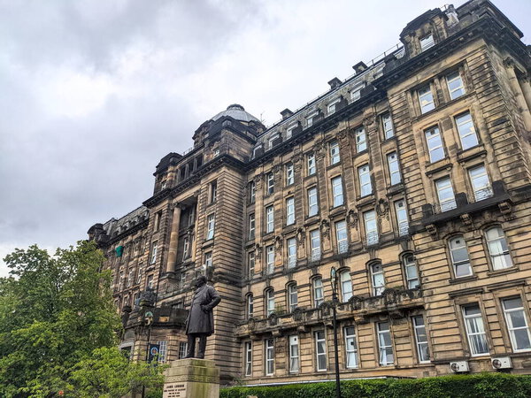 Глазго, Великобритания - 14 июля 2025 года: Низкий угол обзора исторического Королевского лазарета Глазго, здание в стиле Beaux-Arts, со статуей Джеймса Ламсдена на переднем плане под облачным небом