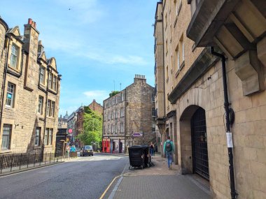 Edinburgh, İngiltere - 17 Temmuz 2025: Sırt çantalı bir kişi açık bir gökyüzü altında geleneksel kumtaşı konut binalarıyla tarihi bir batı limanı boyunca bir kaldırımda yürüyor