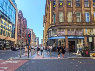 Glasgow, İskoçya - 12 Temmuz 2025: Yayalar, açık mavi gökyüzü altında geleneksel ve modern mimari bir karışım ile çevrili Umut Caddesi 'ndeki bir şehir yaya geçidinde bekliyorlar