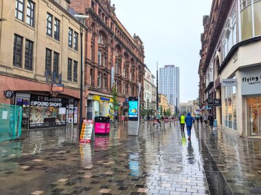 Glasgow, İngiltere - 14 Temmuz 2025: Yayalar, şehir merkezinde bulutlu ve yağmurlu bir günde, popüler bir alışveriş merkezi olan Sauchiehall Caddesi 'nin ıslak ve yansıtıcı kaldırımları boyunca yürürler