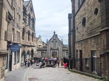 Edinburgh, İskoçya, İngiltere - 17 Temmuz 2025: Turistler tarihi Eski Şehir 'de kaldırımlı bir yay boyunca yürür, bulutlu gökyüzü altında geleneksel taş binalarla sokak sanatına göz atarlar