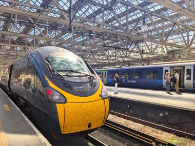 Glasgow, İskoçya - 12 Temmuz 2025: Glasgow Merkez İstasyonu 'nda bir Avanti Batı Yakası treni beklerken, yolcular Viktorya dönemi çelik ve cam çatısının altında bir İskoç Demiryolu treninin yanında bekliyorlar.