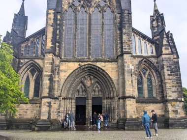 Glasgow, İskoçya - 14 Temmuz 2025: Ziyaretçiler, bulutlu bir gökyüzü altında İskoç Gotik mimarisinin önemli bir örneği olan tarihi Glasgow Katedrali 'nin girişinde toplandılar