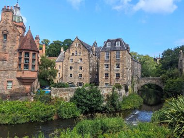 Edinburgh, İskoçya - 16 Temmuz 2025: Dean Village 'ın tarihi Kuyu Mahkemesi ve taş binaları Leith' in sularının kıyıları mavi gökyüzünün altındaki sakin bir vahada.