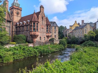 Edinburgh, İskoçya, İngiltere - 16 Temmuz 2025: Tarihi Kuyu Saat Kulesi, Leith nehrinin sakin suları boyunca Dean Village 'da bulunan geleneksel taş binalara bakıyor
