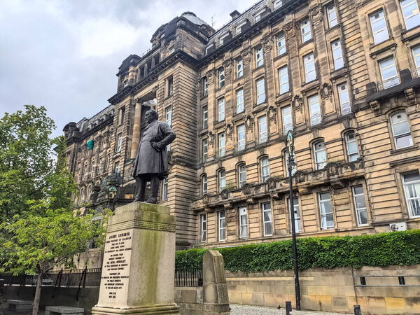 Глазго, Шотландия, Великобритания - 14 июля 2025 года: Выдающаяся статуя Джеймса Ламсдена, стоящая перед исторической Королевской больницей Глазго, накладывает неоклассический фасад под облачным небом