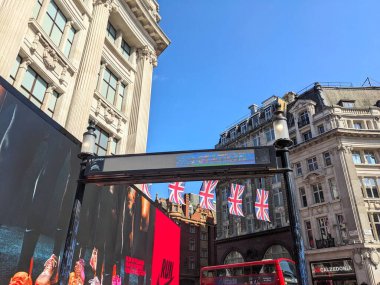 Londra, İngiltere - 09 Ağustos 2025: Oxford Circus London Metro İstasyonu girişinde kırık bir tabela üzerinde Union Jack bayrakları asılı Oxford Circus kavşağındaki kırmızı çift katlı bir otobüsün üzerinde